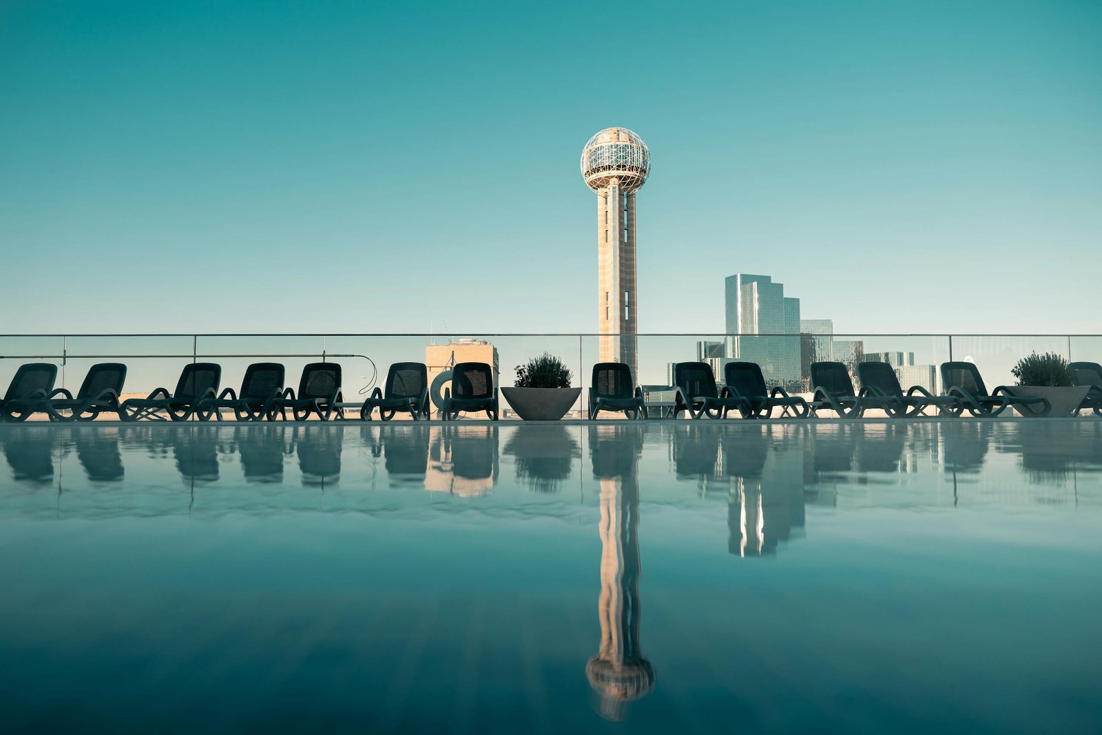 Captivating view of Dallas skyline with Reunion Tower from a rooftop pool at daytime.