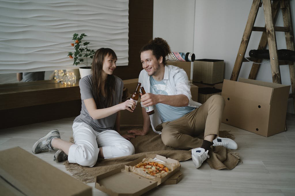 Happy couple enjoying beer and pizza on the floor of their new home together.