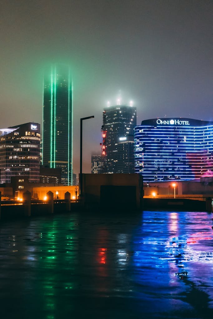 Illuminated Dallas skyline at night with city lights reflecting on wet pavement, creating a vibrant scene.